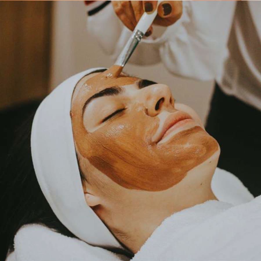A person is lying down with their eyes closed, covered in a white towel. A cosmetic brush is applying a brown facial mask to their face. They are wearing a white headband. 124 on Queen Hotel and Spa | Hotel & Spa Niagara-on-the-lake | 1 (855) 988-4552 A person is lying down with their eyes closed, covered in a white towel. A cosmetic brush is applying a brown facial mask to their face. They are wearing a white headband. 124 on Queen Hotel and Spa | Hotel & Spa Niagara-on-the-lake | 1 (855) 988-4552