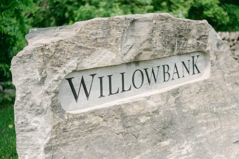 A large stone with the word Willowbank carved into it, surrounded by greenery. 124 on Queen Hotel and Spa | Hotel & Spa Niagara-on-the-lake | 1 (855) 988-4552