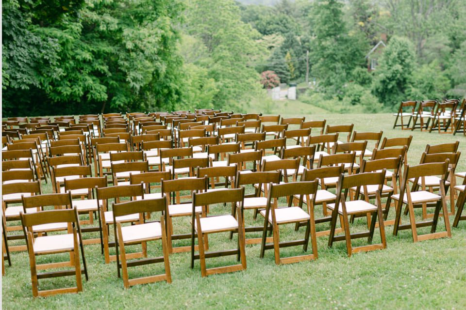 Rows of wooden folding chairs are neatly arranged on a grassy lawn, surrounded by lush green trees. The setup appears to be for an outdoor event or gathering. 124 on Queen Hotel and Spa | Hotel & Spa Niagara-on-the-lake | 1 (855) 988-4552