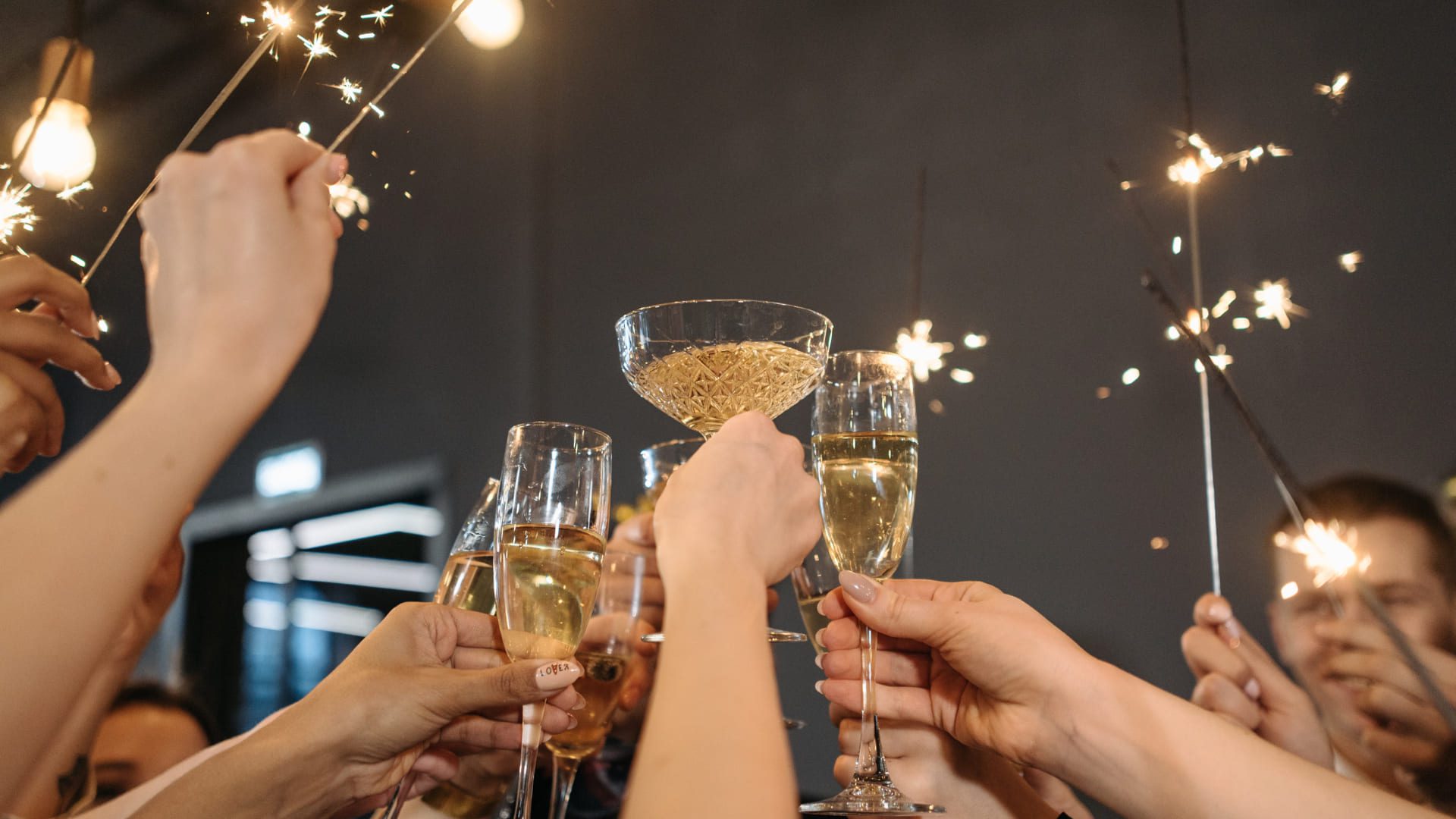 A group of people raising champagne glasses and sparklers in a celebratory toast. The scene conveys a festive atmosphere with a dimly lit background. 124 on Queen Hotel and Spa | Hotel & Spa Niagara-on-the-lake | 1 (855) 988-4552
