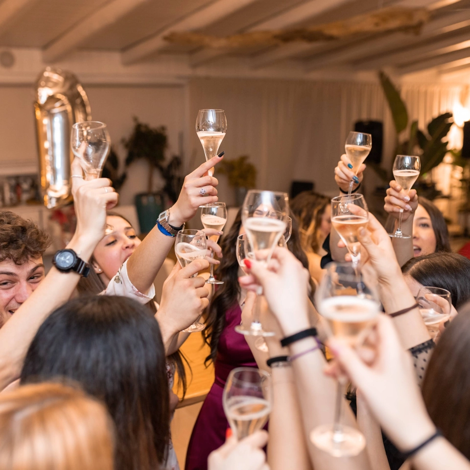 A group of people in a room raising champagne glasses in a celebratory toast. Some are holding balloons. The atmosphere is festive, with people smiling and reaching in from different angles. 124 on Queen Hotel and Spa | Hotel & Spa Niagara-on-the-lake | 1 (855) 988-4552