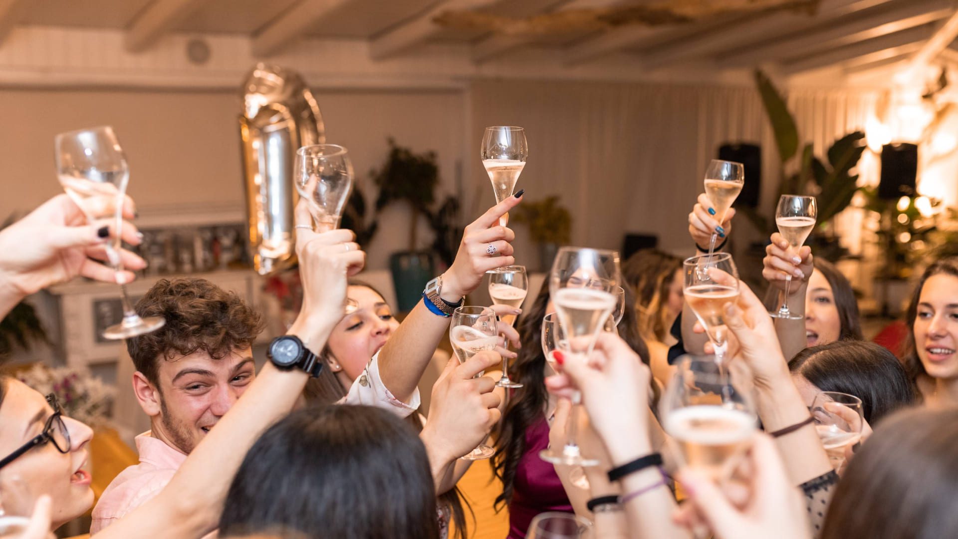 A group of people raise their glasses in a celebratory toast. They are indoors, and the atmosphere is lively. A metallic balloon in the shape of the number 1 is visible in the background. 124 on Queen Hotel and Spa | Hotel & Spa Niagara-on-the-lake | 1 (855) 988-4552
