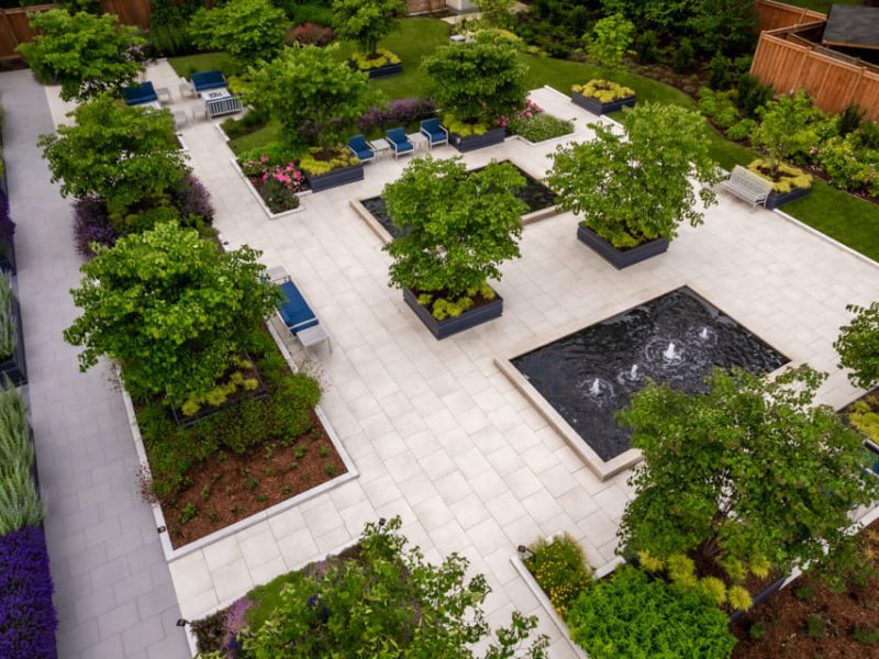 Aerial view of a landscaped garden with geometric pathways, lush greenery, and rectangular water features. Potted trees and benches are arranged around the garden, with vibrant plants adding color. Wooden fences enclose the space. 124 on Queen Hotel and Spa | Hotel & Spa Niagara-on-the-lake | 1 (855) 988-4552