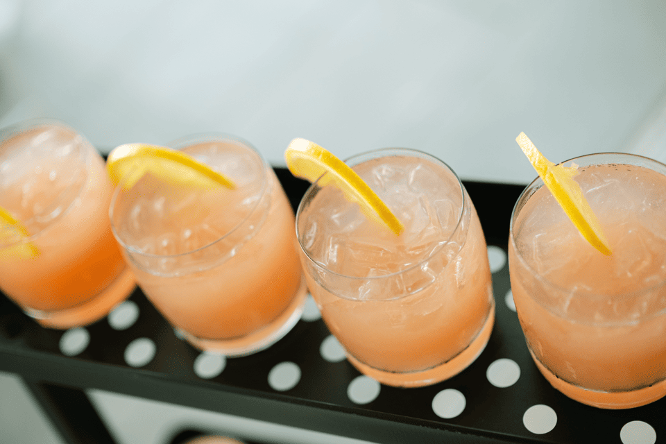 Four glasses of iced pink beverage with lemon slices are arranged in a row on a black tray with white polka dots. The glasses are filled with ice and garnished with a thin lemon wedge each. 124 on Queen Hotel and Spa | Hotel & Spa Niagara-on-the-lake | 1 (855) 988-4552