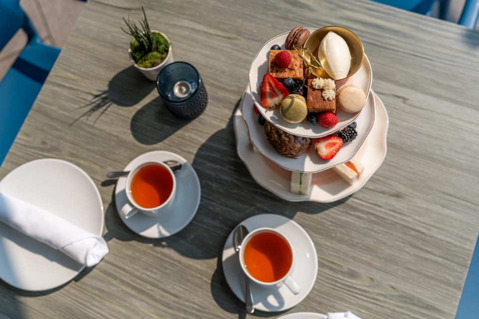 An overhead view of a table set for afternoon tea, featuring two cups of tea and a three-tiered tray with assorted pastries, macarons, berries, and a scoop of ice cream. A candle and small plant are also on the table. 124 on Queen Hotel and Spa | Hotel & Spa Niagara-on-the-lake | 1 (855) 988-4552