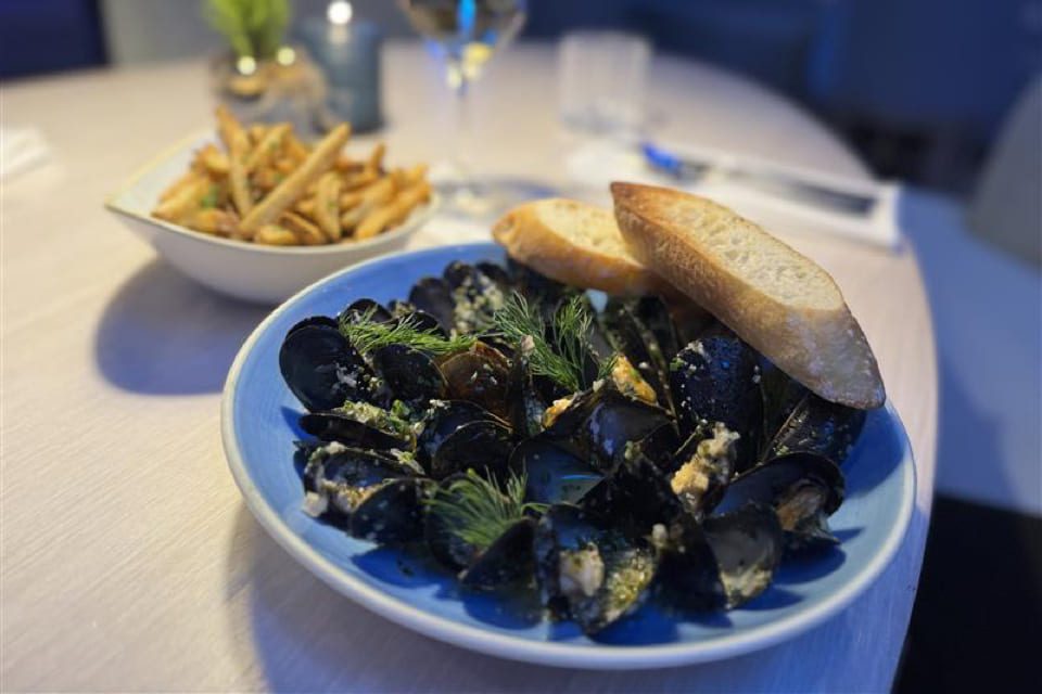 A plate of cooked mussels garnished with herbs and onions is served next to a plate of golden French fries on a marble table. 124 on Queen Hotel and Spa | Hotel & Spa Niagara-on-the-lake | 1 (855) 988-4552