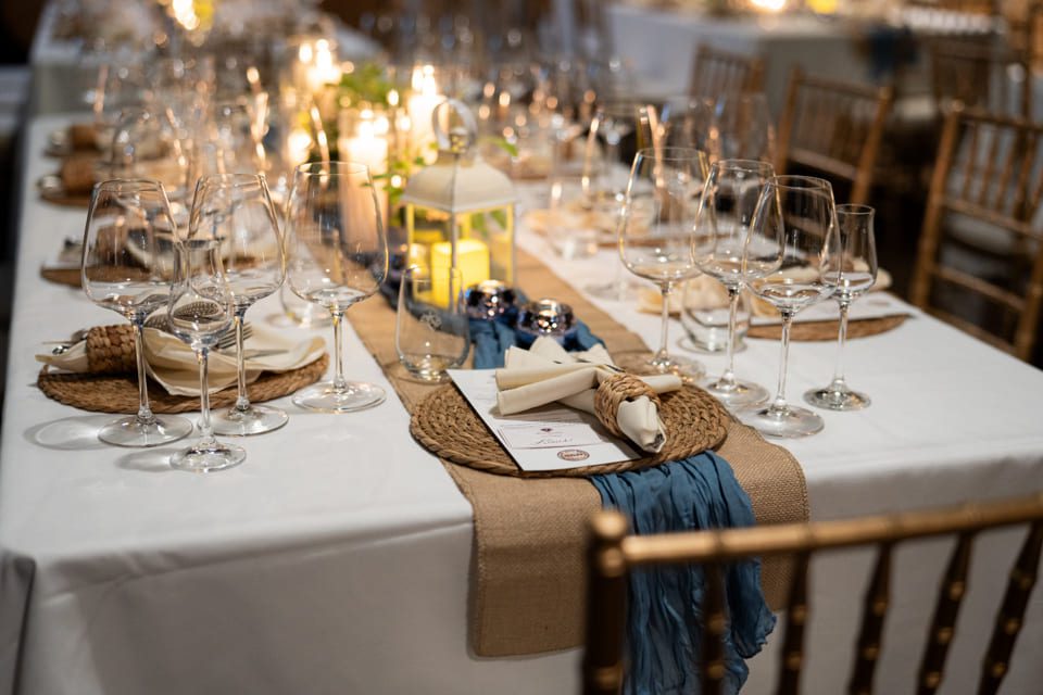 Elegant dinner table set with multiple wine glasses, woven placemats, folded napkins, menus, blue and beige table runner, and a white lantern centerpiece with candles. 124 on Queen Hotel and Spa | Hotel & Spa Niagara-on-the-lake | 1 (855) 988-4552