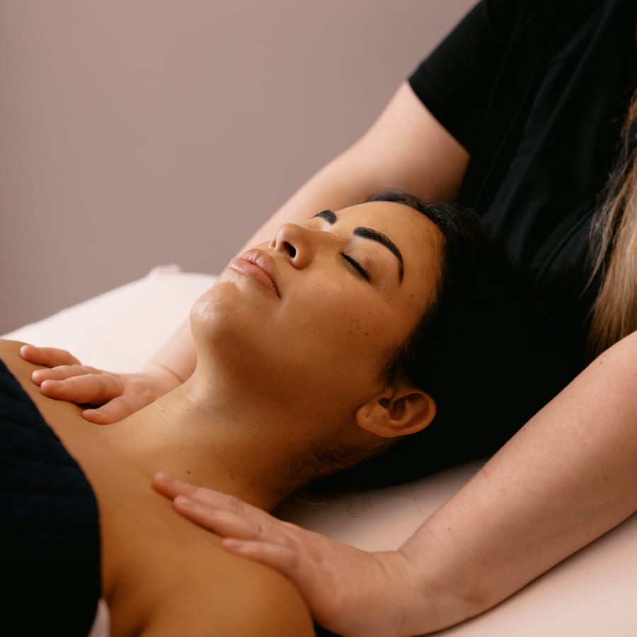 A person lying on a massage table with eyes closed, receiving a gentle shoulder and neck massage from a therapist. 124 on Queen Hotel and Spa | Hotel & Spa Niagara-on-the-lake | 1 (855) 988-4552